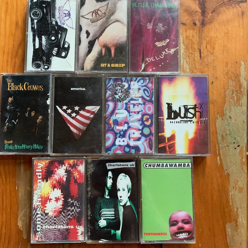 May include: A collection of ten vintage cassette tapes, including albums by The Black Crowes, Bush,  The Charlatans, and  Chumbawamba. The tapes are arranged in two rows on a wooden surface.