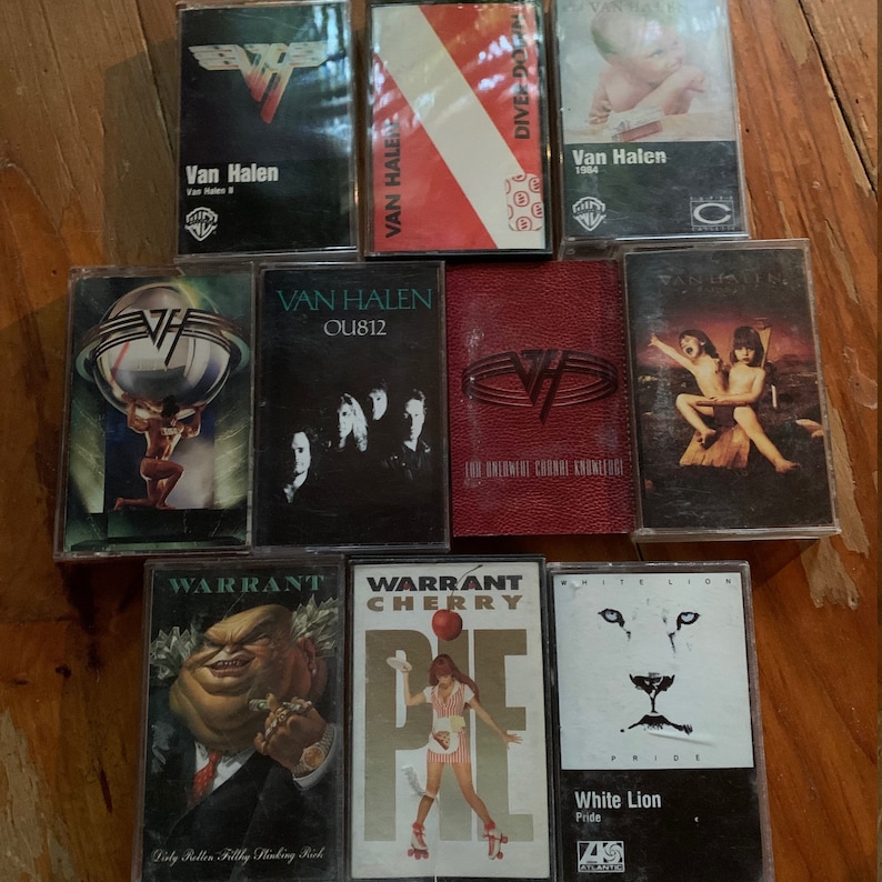 May include: A collection of vintage cassette tapes featuring album art from rock bands Van Halen, Warrant, and White Lion. The tapes display various album covers with band logos, images, and text, including "Diver Down" and "Cherry Pie."