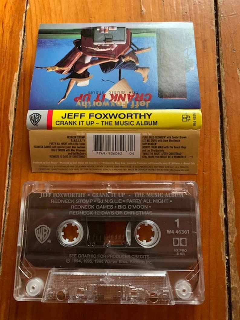 May include: A cassette tape of Jeff Foxworthy's album "Crank It Up - The Music Album". The cassette tape is black with a white Warner Bros. Records logo. The cassette tape is labeled with the album title and the track list: "Redneck Stomp", "S.I.N.G.L.E", "Party All Night", "Redneck Games", "Big O'Moon", and "Redneck 12 Days of Christmas".