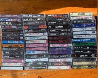May include: A collection of vintage cassette tapes featuring movie soundtracks. The tapes are arranged in rows and include titles such as "The Lost Boys", "Lost Highway", "Platoon", "Pretty Woman", "Rain Man", "Reality Bites", and "Reservoir Dogs".