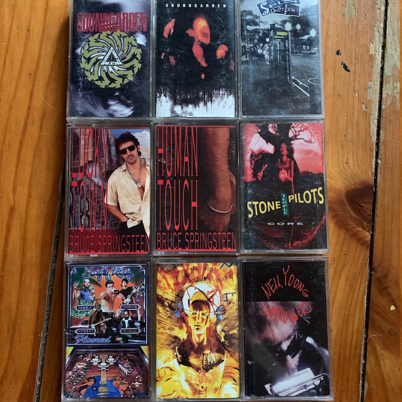 May include: A collection of nine cassette tapes featuring various artists, including Soundgarden, Stone Temple Pilots, Bruce Springsteen, and New Young. The tapes are arranged in three rows of three, with the artist's name and album title visible on each tape.