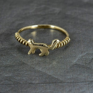 以下が含まれることがあります： 猫が歩いている詳細なシルエットが施された金の指輪。バンドはねじれていて、質感があります。