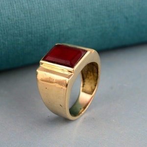 May include: A gold ring with a large, rectangular, red gemstone.