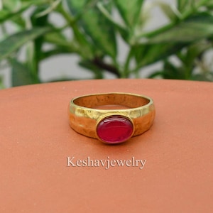 May include: A gold ring with a red oval gemstone. The ring has a textured band.