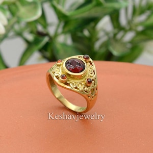 May include: A gold ring with a red gemstone in the center and smaller red gemstones around it. The ring has a detailed design with intricate filigree work.