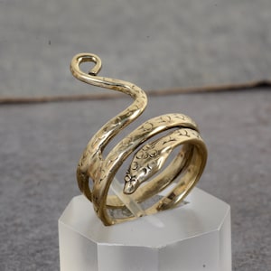 May include: A gold-toned snake ring with a textured surface. The ring is coiled and has a raised head.