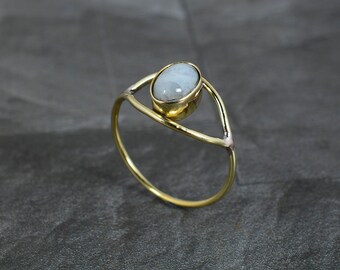 May include: A gold ring with a white oval gemstone set in a delicate, open triangle design.