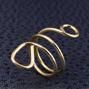 May include: A gold-toned ring with a unique, abstract design. The ring is made of three intertwined bands that form a spiral shape. The top of the ring has a small loop.