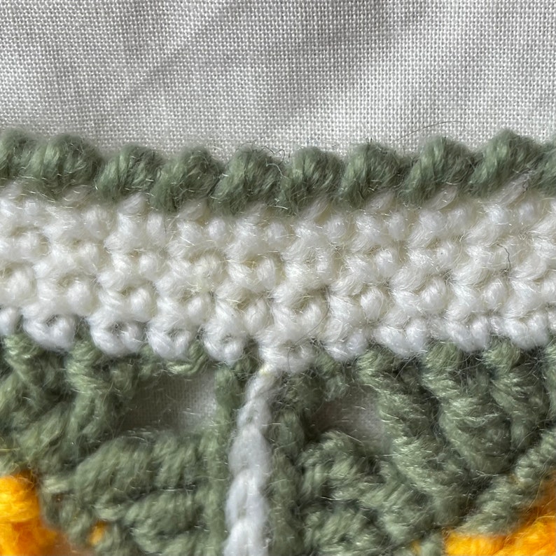 May include: Close-up of a crocheted fabric with a white, green, and yellow colour scheme. The fabric has a textured, bumpy surface.