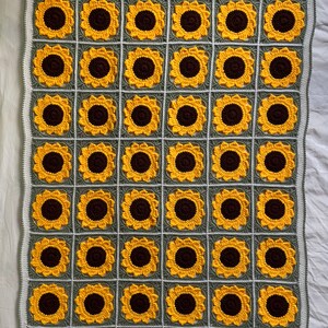May include: A crocheted blanket featuring a sunflower design. The blanket is made from green and yellow yarn and has a repeating pattern of sunflowers with brown centres.