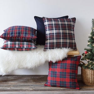 May include: Four plaid throw pillows in red, blue, and white on a white faux fur bench with a small artificial Christmas tree in a wicker basket to the right.