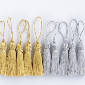 May include: A set of ten tassels, five gold and five silver, with a knotted top and a fringe. The tassels are arranged in two rows, with the gold tassels on top and the silver tassels on the bottom.