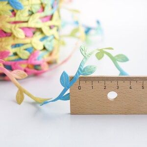 May include: A close-up of a colorful, leafy garland with a wooden ruler measuring 7 inches. The garland is made of paper and features a gradient of blue, green, and yellow leaves.