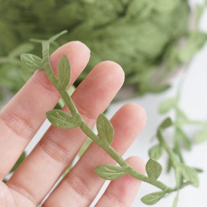 May include: Green leaf garland with a vine-like design. The garland is made of fabric and has a realistic look.