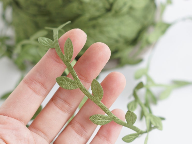 May include: Green leaf garland with a vine-like design. The garland is made of fabric and has a realistic look.