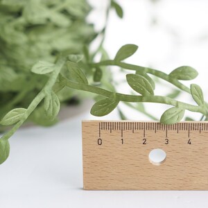 May include: Green paper leaf garland with a ruler for scale. The garland is approximately 6 inches long.