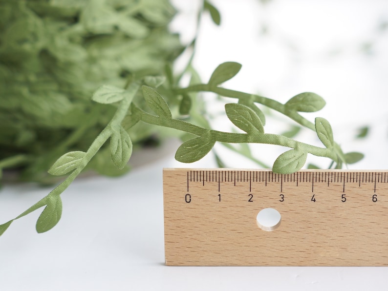 May include: Green paper leaf garland with a ruler for scale. The garland is approximately 6 inches long.