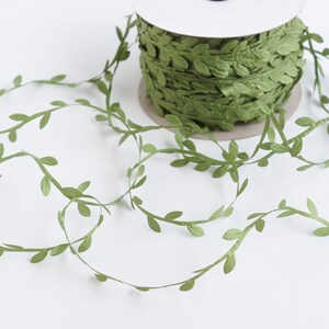 May include: Green leaf garland ribbon, a spool of green ribbon with leaves, perfect for crafting and decorating.