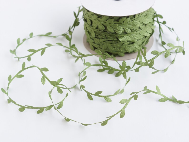 May include: Green leaf garland ribbon, a spool of green ribbon with leaves, perfect for crafting and decorating.