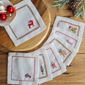 Puede incluir: Conjunto de ocho servilletas de lino blanco con diseños navideños bordados. Cada servilleta presenta un motivo festivo diferente, incluyendo un reno, un osito de peluche, bastones de caramelo, un hombre de jengibre, un cascanueces, Papá Noel y un camión de juguete.