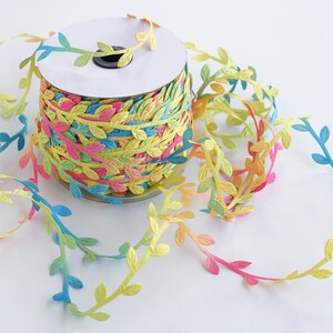 May include: A spool of colorful ribbon with a leafy design. The ribbon is a gradient of pink, yellow, blue, and green.