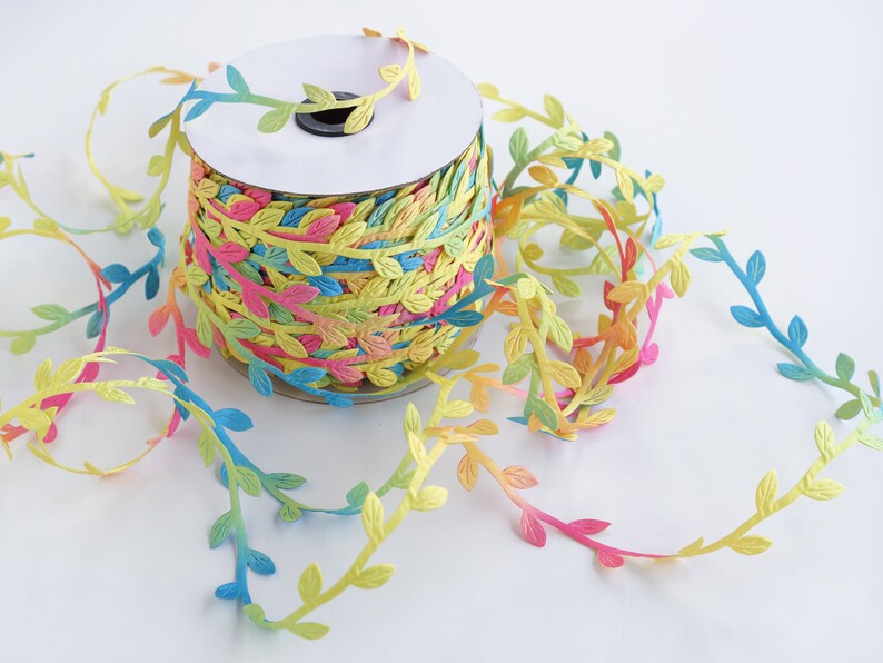 May include: A spool of colorful ribbon with a leafy design. The ribbon is a gradient of pink, yellow, blue, and green.
