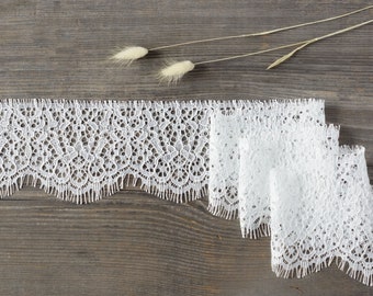 May include: White lace trim with a scalloped edge. The lace is delicate and intricate, with a floral pattern. The trim is perfect for adding a touch of elegance to any project.