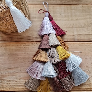 Peut inclure: Un pompon multi-couches avec un schéma de couleurs blanc, bordeaux, or et gris clair. Le pompon est fait de fils doux et soyeux et a une apparence délicate et faite à la main.