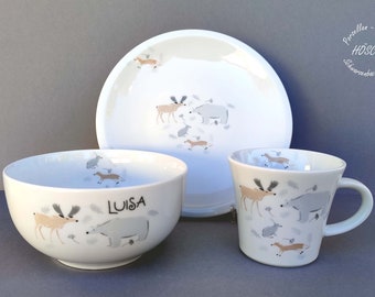 May include: A white ceramic children's dinnerware set with a woodland animal theme. The set includes a bowl, a plate, and a mug. The bowl and mug feature the name "LUISA" printed on them. The plate, bowl, and mug all feature a design of a moose, a bear, a rabbit, and a fox.