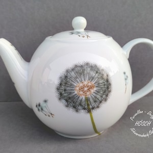 Könnte beinhalten: Weiße Keramik-Teekanne mit einem Löwenzahn-Design. Die Teekanne hat einen runden Körper, einen gebogenen Ausguss und einen Schlaufengriff. Der Löwenzahn ist in Grau-, Braun- und Grüntönen dargestellt. Die Teekanne hat einen Deckel mit einem kleinen Knopf.