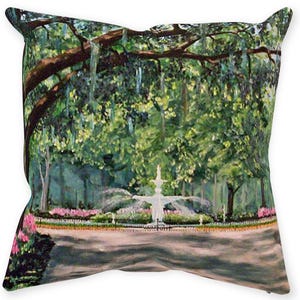 May include: Square decorative pillow featuring a park scene with a white fountain, lush green trees, and pink flowers. The artwork has a painterly style, with visible brushstrokes and a soft color palette. The pillow is a home decor item.