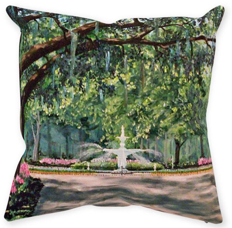 May include: Square decorative pillow featuring a park scene with a white fountain, lush green trees, and pink flowers. The artwork has a painterly style, with visible brushstrokes and a soft color palette. The pillow is a home decor item.