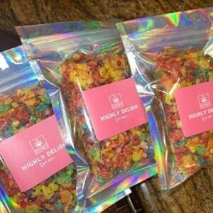 May include: Three clear plastic bags with colorful cereal treats inside. Each bag has a pink label with the text "HIGHLY DELISH EAT ME!" printed on it.