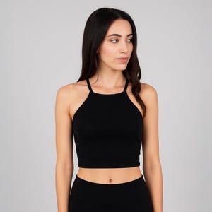 May include: A black halter crop top with a high neckline. The top has thin straps and a fitted silhouette. The fabric appears to be a smooth, solid colour. The top is paired with black bottoms.