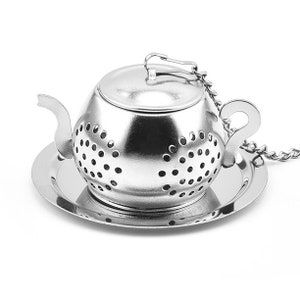 May include: A stainless steel tea infuser shaped like a teapot, with a lid and a small saucer. The infuser has a chain attached and is perforated with small holes for steeping tea leaves. The teapot infuser is designed for loose leaf tea.