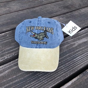 May include: Blue and beige baseball cap with the text "NEW ORLEANS YARD DOG" and an alligator graphic.