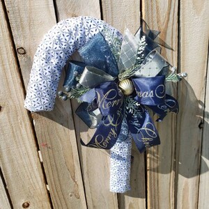 May include: A blue and white candy cane Christmas wreath with a large blue bow and gold lettering that says "Merry Christmas".