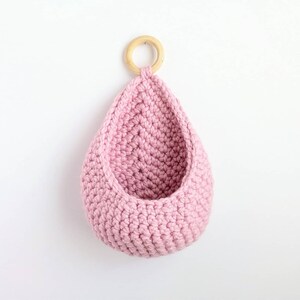 May include: A pink crocheted hanging basket with a wooden ring at the top.