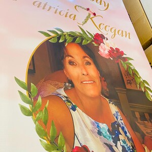 May include: A pink and white birthday banner with gold lettering that reads "Happy 50th Birthday Patricia Keegan". A woman is pictured in a floral frame with green leaves and pink and red flowers.