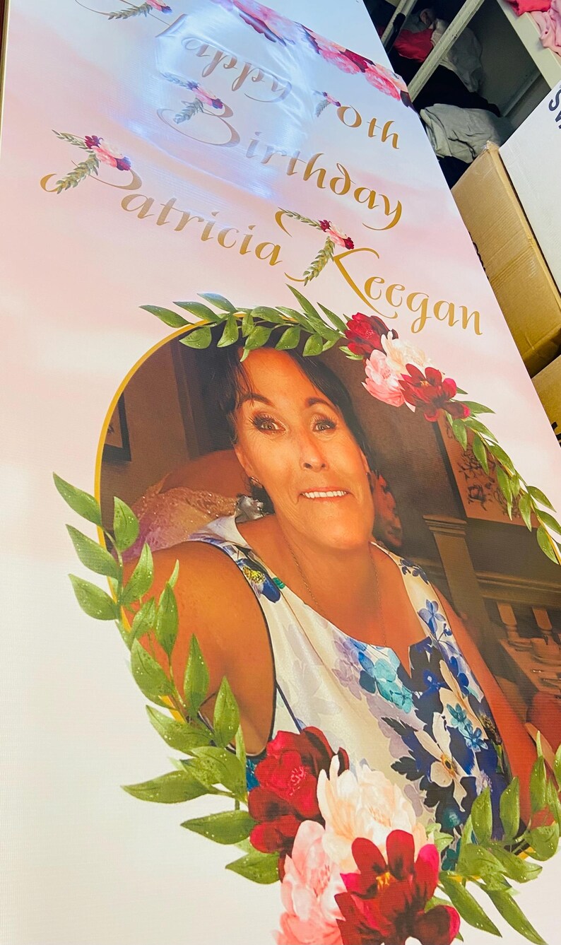 May include: A pink and white birthday banner with gold lettering that reads "Happy 50th Birthday Patricia Keegan". A woman is pictured in a floral frame with green leaves and pink and red flowers.