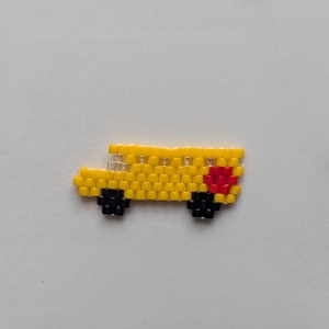 May include: A yellow school bus made of small beads with black wheels and a red heart on the side.