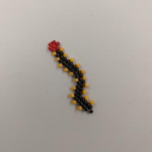 May include: A beaded snake charm with a red head, black body, and yellow accents.