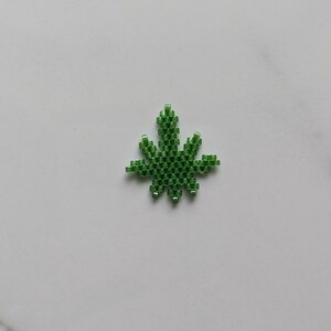 May include: A green beaded marijuana leaf charm, a popular symbol of the cannabis culture.