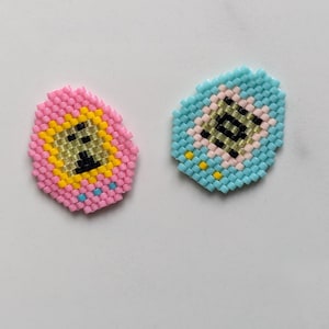 May include: Two small pixelated keychain charms, one pink and one blue, with a black and white pixelated design inside.