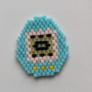 May include: A blue and yellow beaded egg with a pink and black face. The face has a black eye and a yellow mouth.