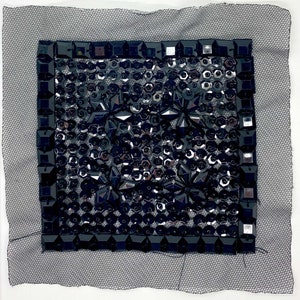 Op de afbeelding: Een zwarte vierkante patch van pailletten en strass op een zwarte mesh-stof achtergrond.