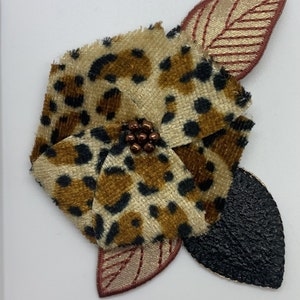 May include: A brown and black leopard print fabric flower with brown beads in the centre and two gold and red leaves.
