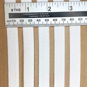 May include: White elastic with brown stripes. The elastic is measured with a ruler showing 3 inches.