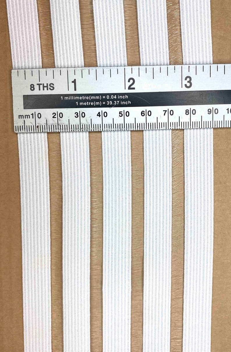 May include: White elastic with brown stripes. The elastic is measured with a ruler showing 3 inches.