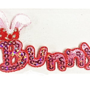 Könnte beinhalten: Rosa und roter Pailletten-Aufnäher zum Aufbügeln mit dem Wort "Bunny" und einem rosafarbenen Hasenohren-Design.
